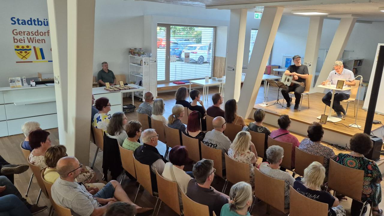 auf der Bühne die beiden Künstler, davor das begeisterte Publikum, im Hintergrund der Büchertisch von "Bücher am Spitz" 