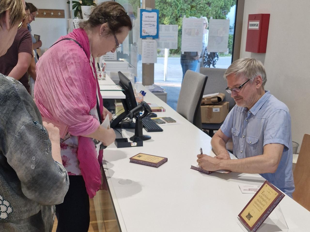 Stefan Franke signiert eines seiner Bücher, davor steht eine Frau, die das Buch gekauft hat