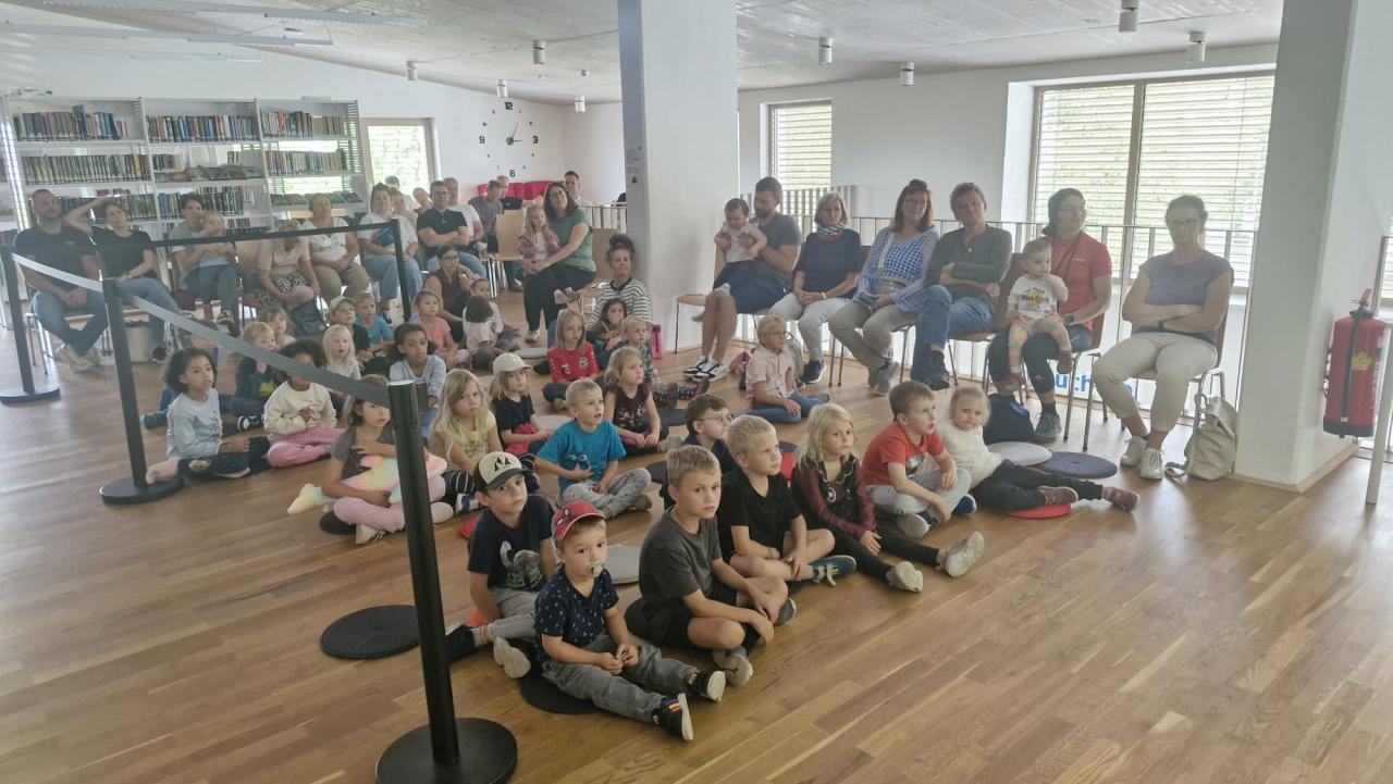 Kinder sitzen am Boden, Erwachsene am Rand auf Sesseln
