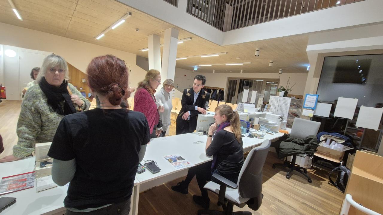 mehrere Menschen unterhalten sich stehend, 1 Person sitzt