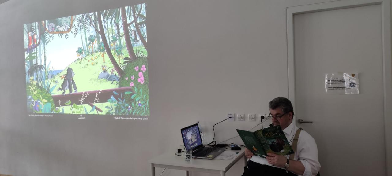 ein Mann sitzt und liest ein Buch, an der Wand das Bild dazu