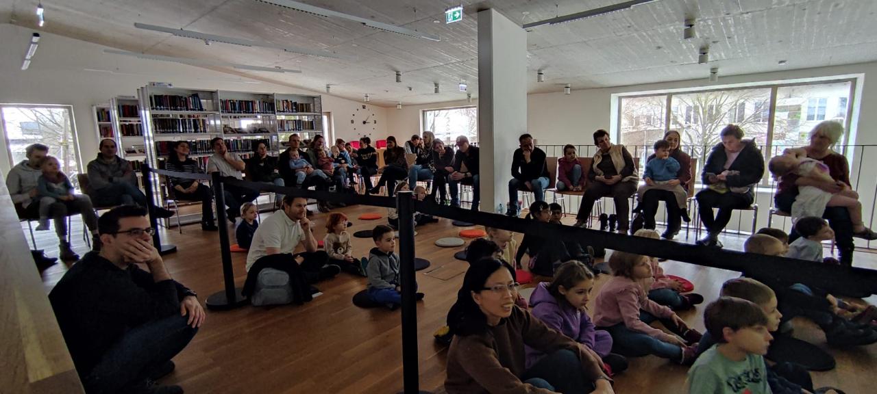 Kinder sitzen am Boden, Erwachsene am Rand auf Sesseln