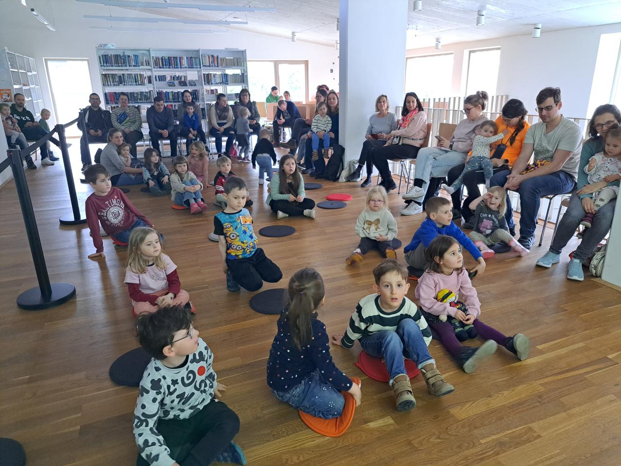 Kinder sitzen am Boden, die Erwachsene auf den Sesseln rundherum