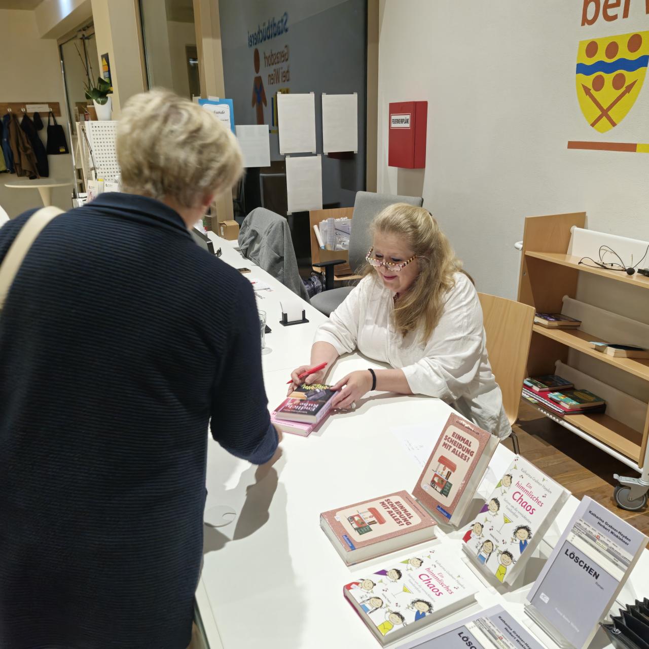 die Autorin sitzt bei Tisch und signiert ihre Bücher